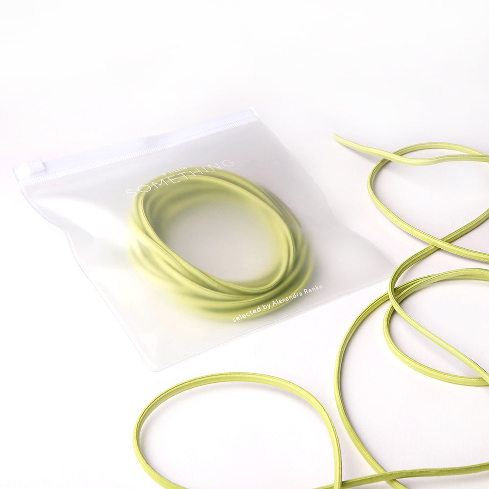 Ein aufgerolltes grünes Alexandra Renke Elastikband, teilweise in einer gefrosteten Reißverschlusstasche mit extra Kordel außen, ruht auf einer weißen Fläche - perfekt für Ihr nächstes Bastelprojekt.