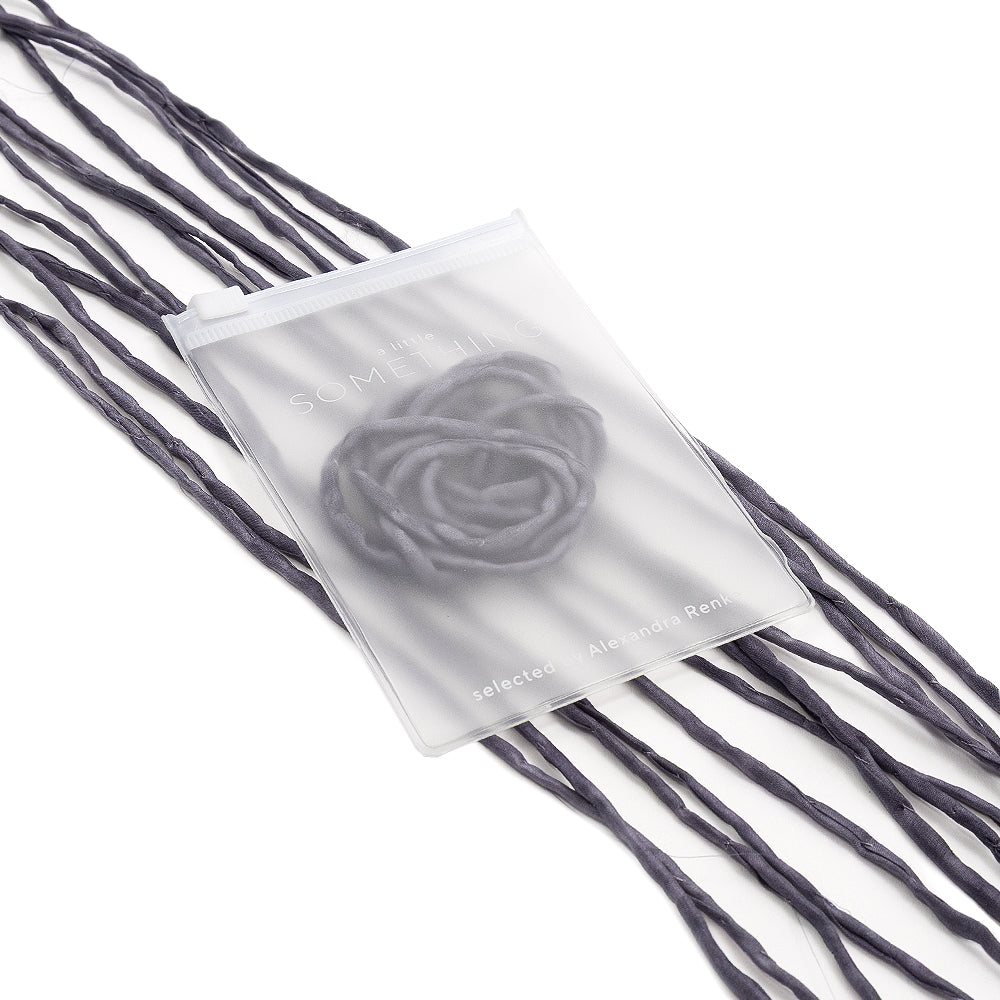 Ein mattierter Beutel von ☆, handgenäht und innen mit einer zarten Blume verziert, ruht auf einer verflochtenen dunklen Seidenschnur vor einem weißen Hintergrund.