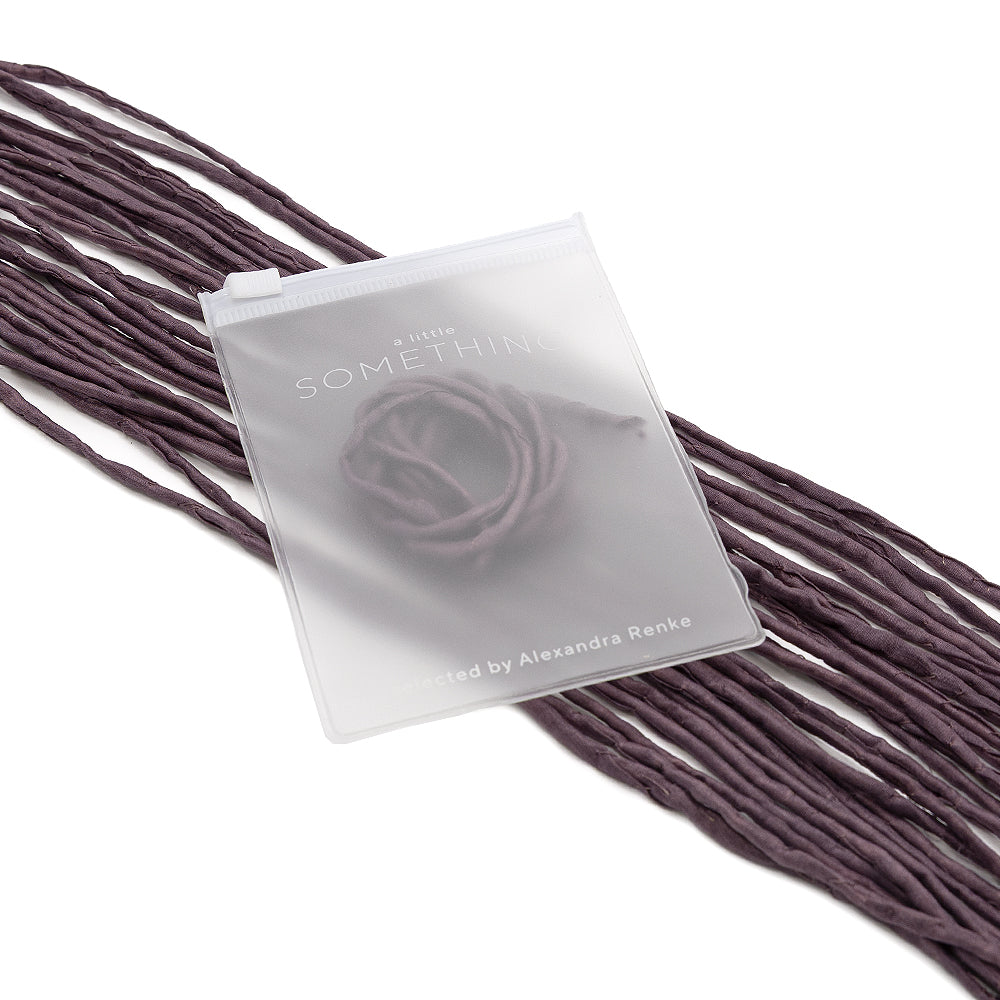 Ein mattierter Plastikbeutel von ☆ mit der Aufschrift „A Little Something“ hängt an violetten Seidenschnur-Bändern und eignet sich somit hervorragend als Geschenkverpackung.