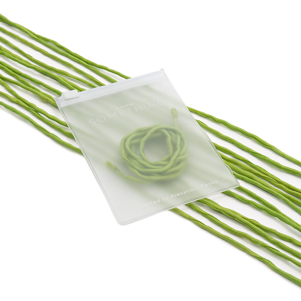 Ein mattes Säckchen von ☆ mit handgenähten grünen Kordeln im Inneren, umgeben von einer losen Seidenschnur, vor weißem Hintergrund.