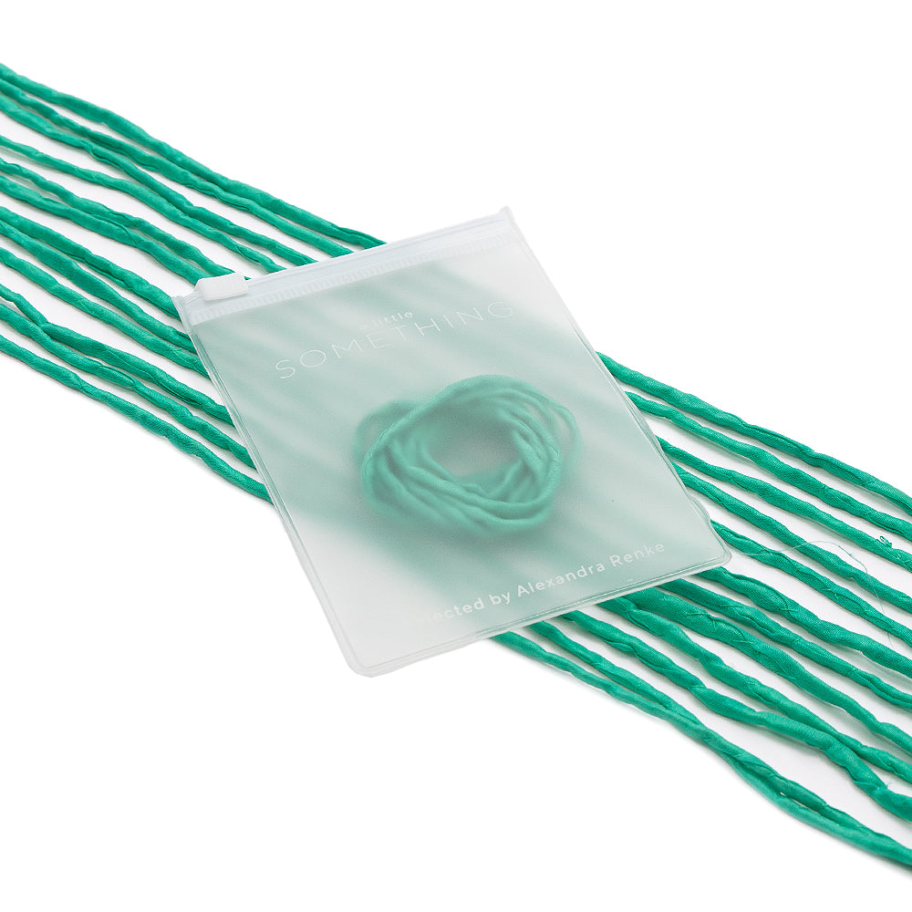 ☆ Grüne Kordeln aus Seidenschnur, kombiniert mit einem durchscheinenden, handgenähten Beutel mit den Aufschriften „SOMETHING“ und „Alexandra Renke“ – ideal für stilvolle Geschenkverpackungen – alles elegant vor weißem Hintergrund präsentiert.