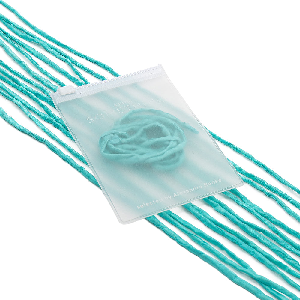 Ein durchscheinender Beutel mit türkisfarbenen Seidenschnur-Fäden und einer Rosette im Inneren, handgenäht, von ☆, auf einer weißen Unterlage liegend – eine elegante Wahl für Geschenkverpackungen.