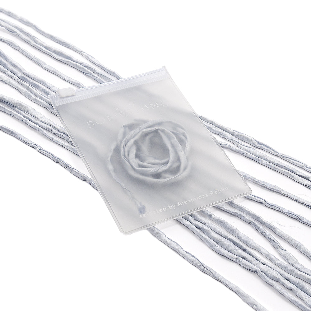 Ein durchscheinender Beutel von ☆, in dem sich ein aufgerollter hellblauer Schal befindet, verziert mit losen Stofffäden aus passendem Material und elegant mit einer Seidenschnur veredelt – ideal für außergewöhnliche Geschenkverpackungen oder als zartes, handgenähtes Accessoire.