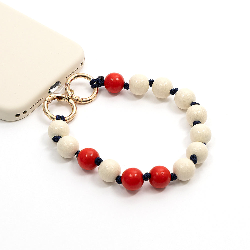 Ein beiges ☆ Smartphone, das an einem Armband befestigt ist, das aus runden, abwechselnd roten und weißen Holzperlen an einer marineblauen Flechtkordel gefertigt ist.