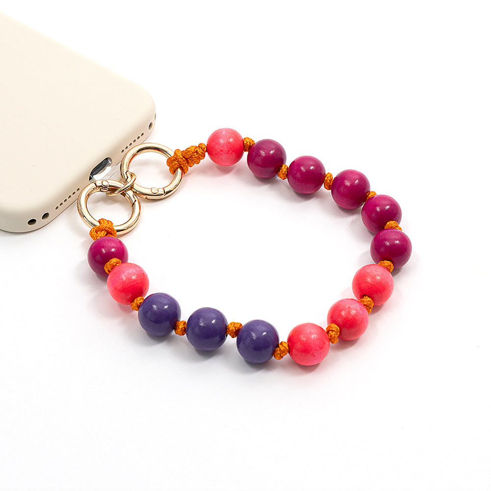 ☆ Perlen-Handyband mit rosa und lila Perlen sowie orangefarbenen Nylonknoten, das mit goldenen Ringen am Gerät befestigt ist, dargestellt auf weißem Hintergrund.
