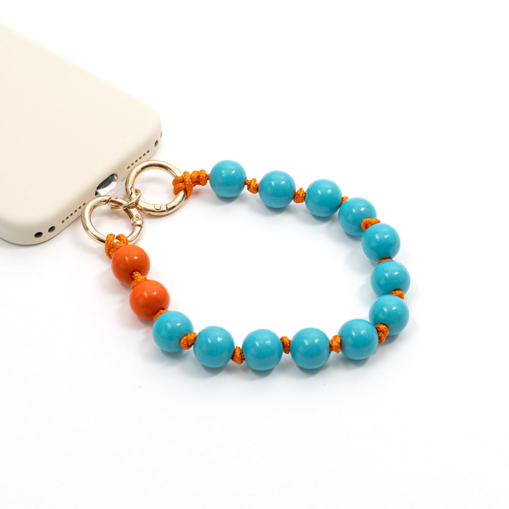 Ein ☆-Handy mit einem Makramee-Perlenarmband, bestehend aus blauen und orangefarbenen Perlen, die durch goldene Ringe miteinander verbunden sind, vor einem weißen Hintergrund.