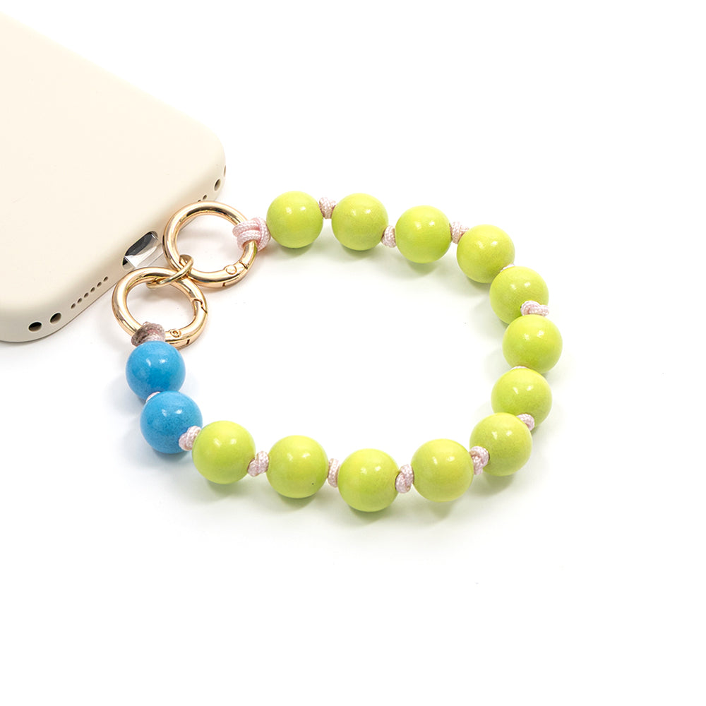 Eine ☆ Handyhülle, die an einem runden Armband mit Perlen befestigt ist. Sie besteht aus strapazierfähigem Nylon und ist mit einer limettengrünen sowie zwei blauen Perlen auf weißem Hintergrund verziert.