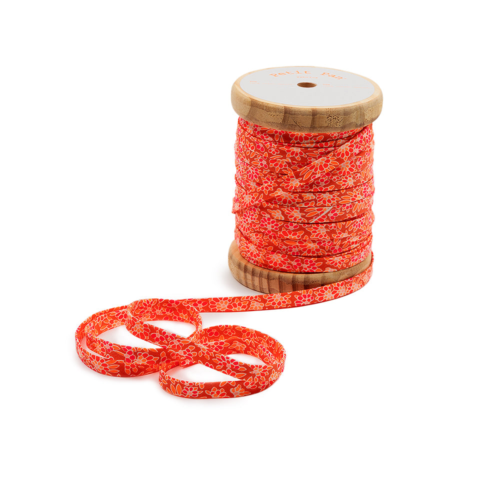 Eine Rolle mit rotem Blumenband, ideal für Nähprojekte, wobei ein Teil des Bandes abgewickelt und auf einem weißen Hintergrund zu einer Schleife gebunden ist.
