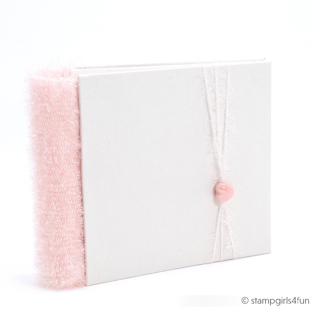 Quadratisches weißes Album mit einem pelzigen rosa Rücken, gebunden mit einer Schnur und einem rosa Knopf auf der Vorderseite - hergestellt mit Rico Design Creative Bubble Garn für eine einzigartige, strukturierte Oberfläche.