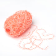 Ein Strang des pfirsichfarbenen Rico Design Creative Bubble Yarn mit einem losen Faden liegt auf einem weißen Hintergrund - perfekt, um einzigartige Geschirrtücher zu häkeln.
