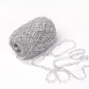 Ein Knäuel silberglänzendes Rico Design Creative Bubble Garn mit einem losen Strang auf weißem Grund - ideal zum Häkeln oder für einzigartige Schrubber.