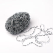 Ein Knäuel Creative Bubble Garn in Metallic-Silber von Rico Design, mit einer flauschigen Struktur und teilweise aufgedreht auf weißem Grund - ideal zum Häkeln von lustigen Geschirrtüchern.