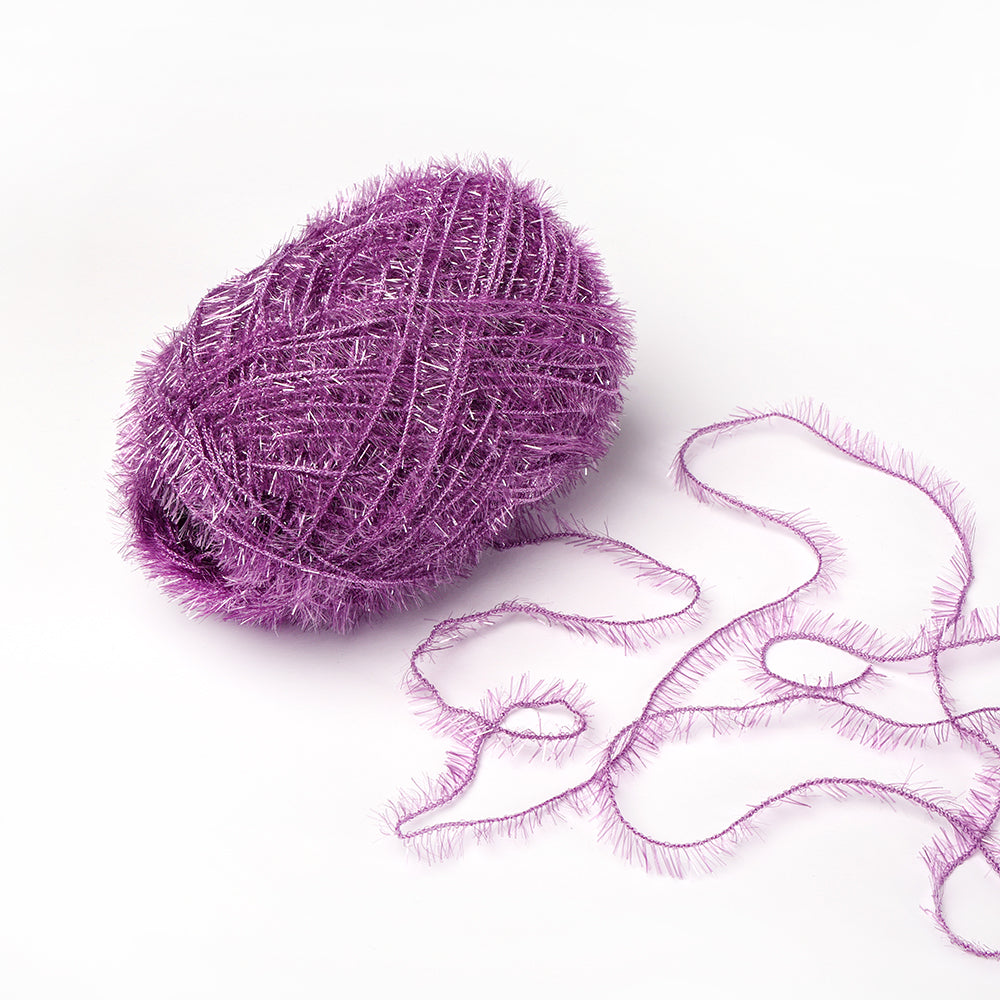 Eine glitzernde lilafarbene Rico Design Creative Bubble Garn-Kugel mit einem losen, flauschigen Faden erstreckt sich auf einer weißen Oberfläche - ideal, um Schwämme (Spüllappen) zu häkeln und Ihren Häkelprojekten eine lustige Textur zu verleihen.
