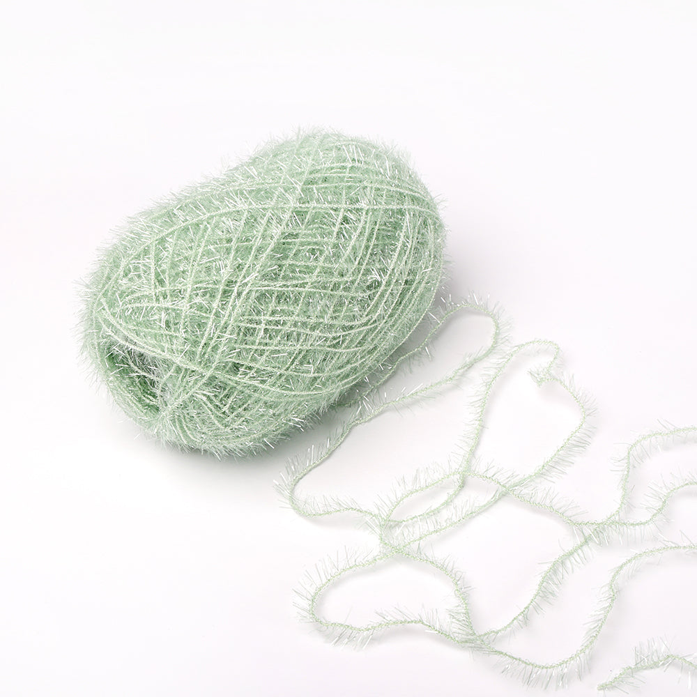 Ein Knäuel des blassgrünen, flauschigen Garns Rico Design Creative Bubble Garn, ideal zum Häkeln von Geschirrtüchern, mit einem losen Strang auf weißem Grund.