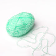 Ein Knäuel des hellgrünen, flauschigen Rico Design Creative Bubble Garns mit einem losen Faden ruht auf einem weißen Hintergrund - dank seiner strapazierfähigen Faser ideal zum Häkeln von Geschirrtüchern.