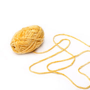 Ein gelbes Knäuel Rico Design Chenille Garn mit einem losen Faden auf weißem Grund, ideal für die Herstellung von Kuschelfiguren oder als Häkelgarn für Ihr nächstes kuscheliges Projekt.