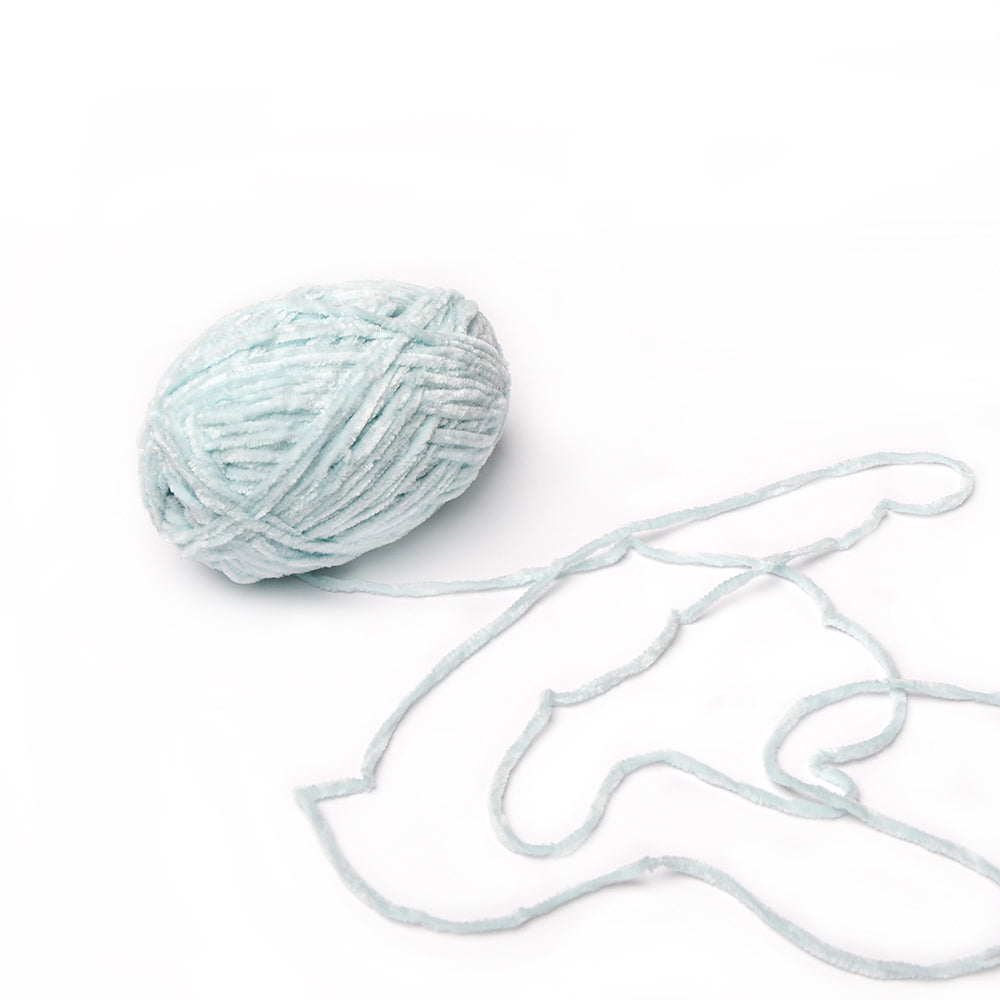 Ein Knäuel aus hellblauem, superflauschigem Garn von Rico Design mit einer Chenille-Struktur und einem losen Strang, der sich auf weißem Grund ausbreitet.