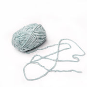 Ein hellblauer Ball aus superflauschigem Garn von Rico Design mit Chenille-Struktur und einem losen Strang, perfekt zum Häkeln, auf weißem Hintergrund.
