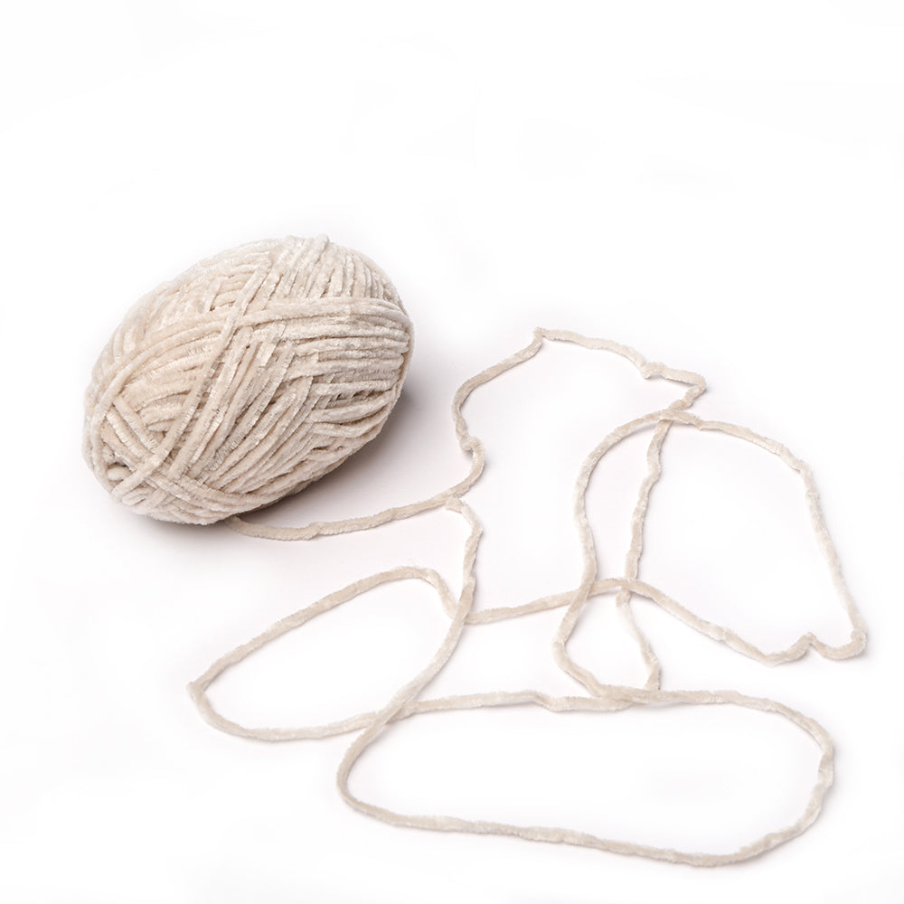 Ein Knäuel aus cremefarbenem Rico Design Häkelgarn mit einem losen Strang, der sich anmutig auf weißem Hintergrund abwickelt.