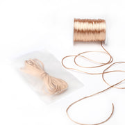 Eine Spule mit beigen Satinkordeln von Alexandra Renke und eine versiegelte Plastiktüte mit einem vorgeschnittenen Bündel derselben Kordel – ideal für DIY-Wohnaccessoires oder zur Herstellung von einzigartigem Schmuck.