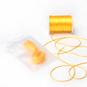 Neben einer Spule mit gelber Satinkordel von Alexandra Renke, die sich ideal zum Schmuckherstellen oder für DIY-Wohnaccessoires eignet, liegt eine halbtransparente Tüte mit weiteren leuchtend gelben Satinkordeln.