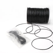 Eine Spule schwarzer gewachster Baumwollkordel von Alexandra Renke, mit einem Abschnitt in einer durchsichtigen Plastiktüte, ideal für Schmuckherstellung oder Dekoration, ausgestellt auf weißem Hintergrund.