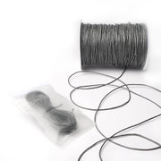 Eine Spule grau gewachste Baumwollkordel von Alexandra Renke, etwas abgewickelte Kordel und ein kleineres Bündel in einem durchsichtigen Beutel - ideal für Schmuckherstellung oder Dekorationsprojekte.