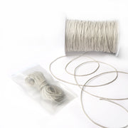 Eine Spule und ein kleines Bündel beigefarbener, gewachster Baumwollkordel von Alexandra Renke mit losen Strängen auf weißem Hintergrund, ideal für Dekoration oder Schmuckherstellung.