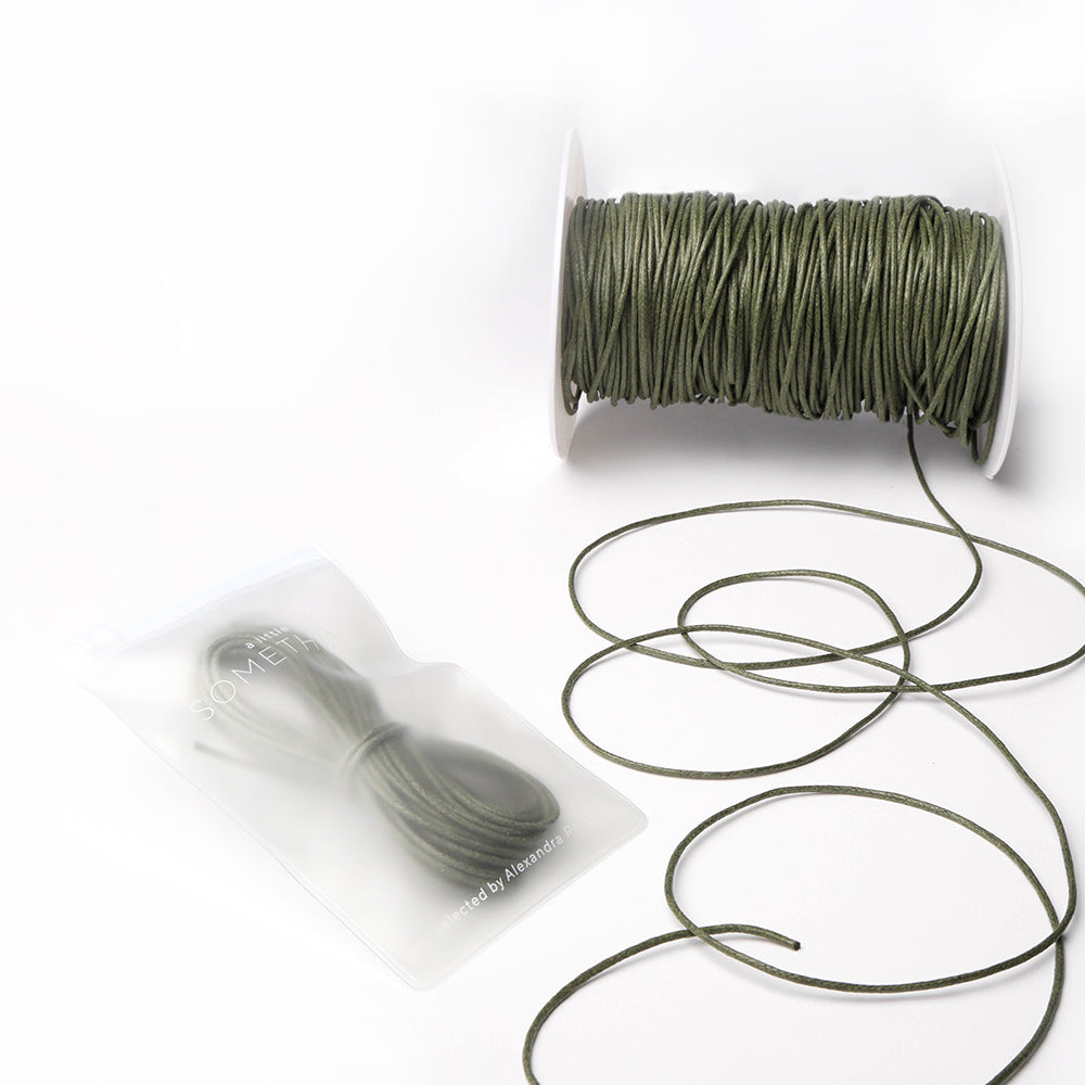 Alexandra Renke olivgrüne gewachste Baumwollkordel auf einer Spule, mit einer kleinen Kordellänge in einem durchsichtigen Beutel - ideal für Dekoration oder Schmuckherstellung.