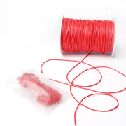 Eine Spule rot gewachste Baumwollkordel von Alexandra Renke, mit etwas loser Kordel und einem kleinen Beutel mit extra Kordel - ideal für Schmuckherstellung oder kreative Dekorationsprojekte.