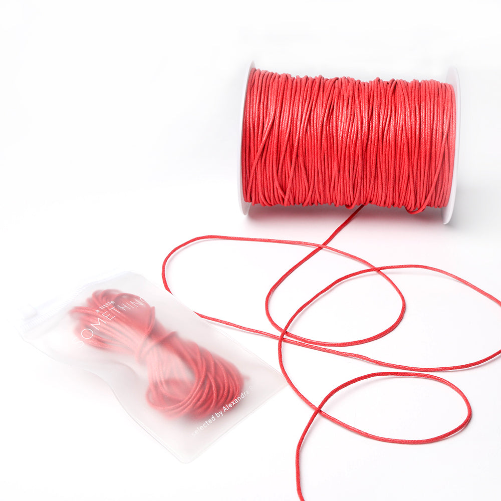 Eine Spule rot gewachste Baumwollkordel von Alexandra Renke, mit etwas loser Kordel und einem kleinen Beutel mit extra Kordel - ideal für Schmuckherstellung oder kreative Dekorationsprojekte.