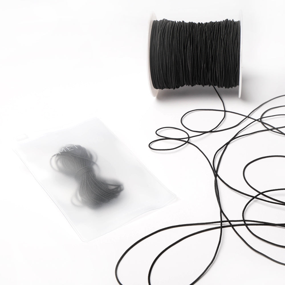 Eine Spule mit schwarzer Schnur und ein Bündel Alexandra Renke Elastikband in einem durchsichtigen Plastikbeutel liegen auf einer weißen Fläche - ideal für Ihr nächstes Bastelprojekt.