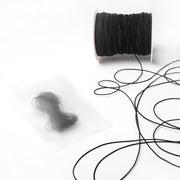 Eine Spule mit schwarzer Schnur und ein Bündel Alexandra Renke Elastikband in einem durchsichtigen Plastikbeutel liegen auf einer weißen Fläche - ideal für Ihr nächstes Bastelprojekt.