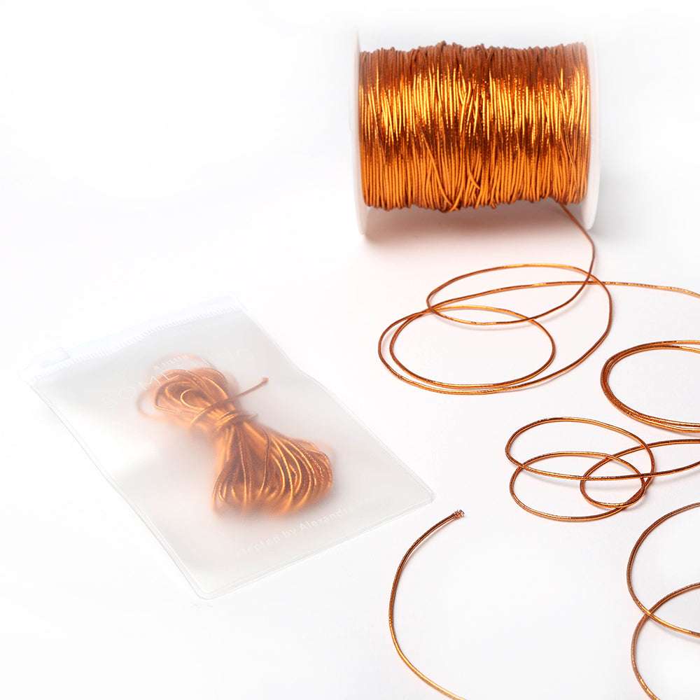 Eine Spule mit glänzender Kupferkordel mit losen Strängen und eine gebündelte Kordel von Alexandra Renke, verpackt in einem durchsichtigen Beutel - perfekt für jedes Bastelprojekt.