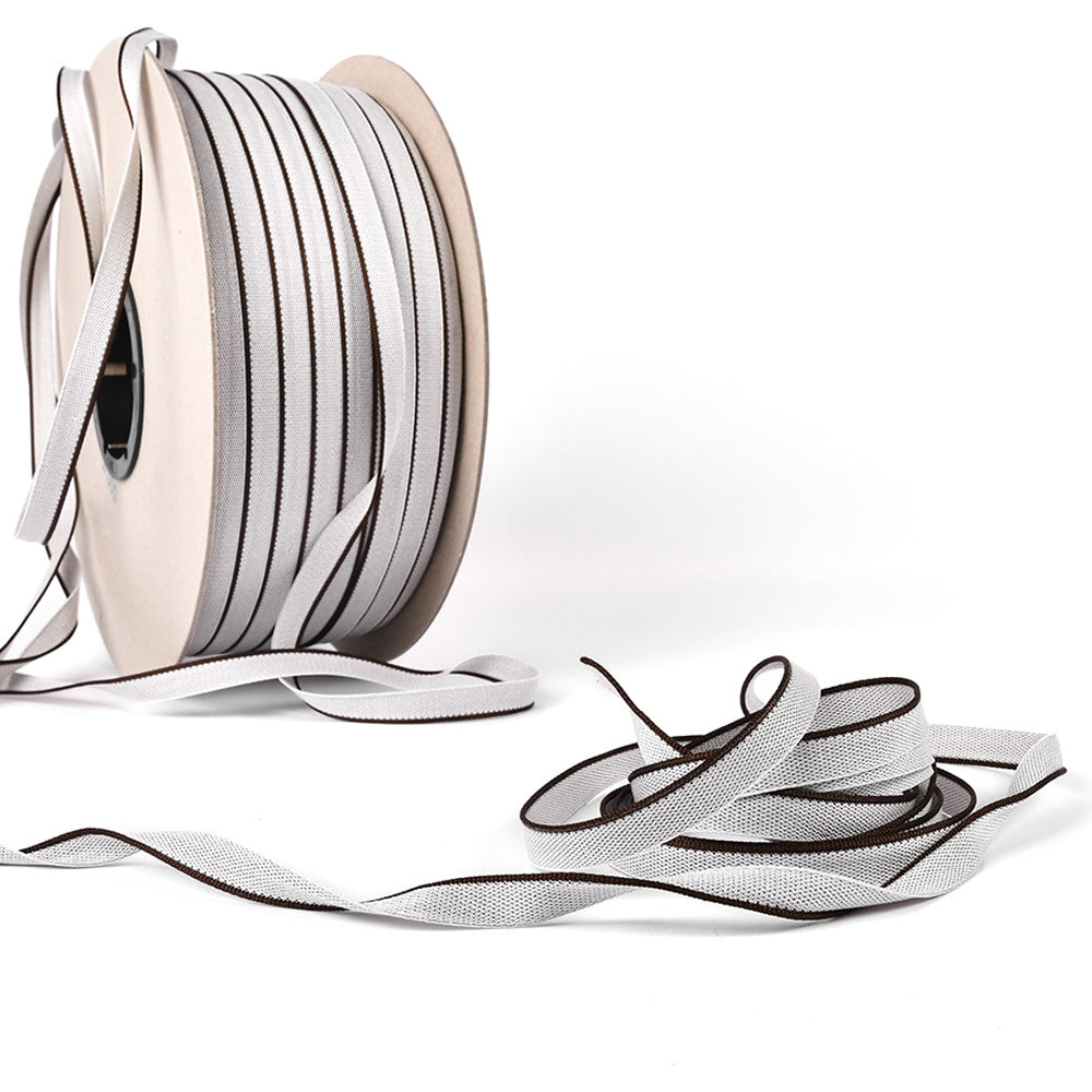 Zwei Rollen Alexandra Renke Kapitalband grau reflektierend mit schwarzem Rand, perfekt für Hardcover-Buchrücken - eine Rolle aufrecht, die andere abgewickelt und aufgewickelt.