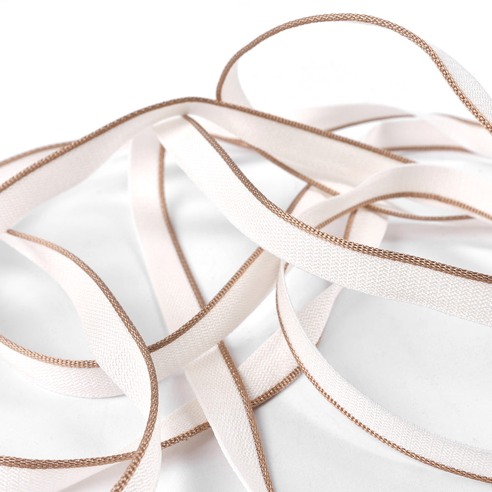 Zartrosafarbene, flache Kapitalband-Bänder mit braunen Rändern von Alexandra Renke, die häufig für Hardcover-Bücher verwendet werden, liegen locker verknotet auf einer weißen Fläche.