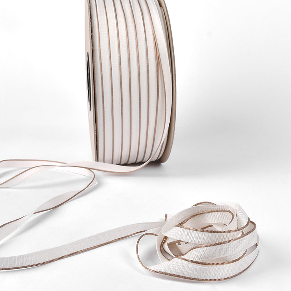 Eine Spule weißes Alexandra Renke Kapitalband mit beigen Rändern, teilweise auf weißer Oberfläche abgewickelt - ideal zum Befestigen von Buchrücken in Hardcover-Buchprojekten.