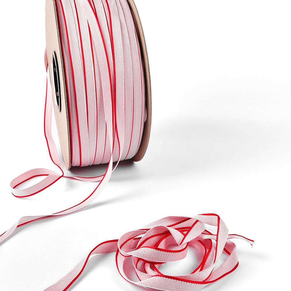 Eine Spule mit weißem Alexandra-Renke-Band mit rotem Rand, ähnlich dem Kapitalband, das in gebundenen Büchern verwendet wird, mit einem losen Band, das daneben auf weißem Hintergrund aufgewickelt ist.