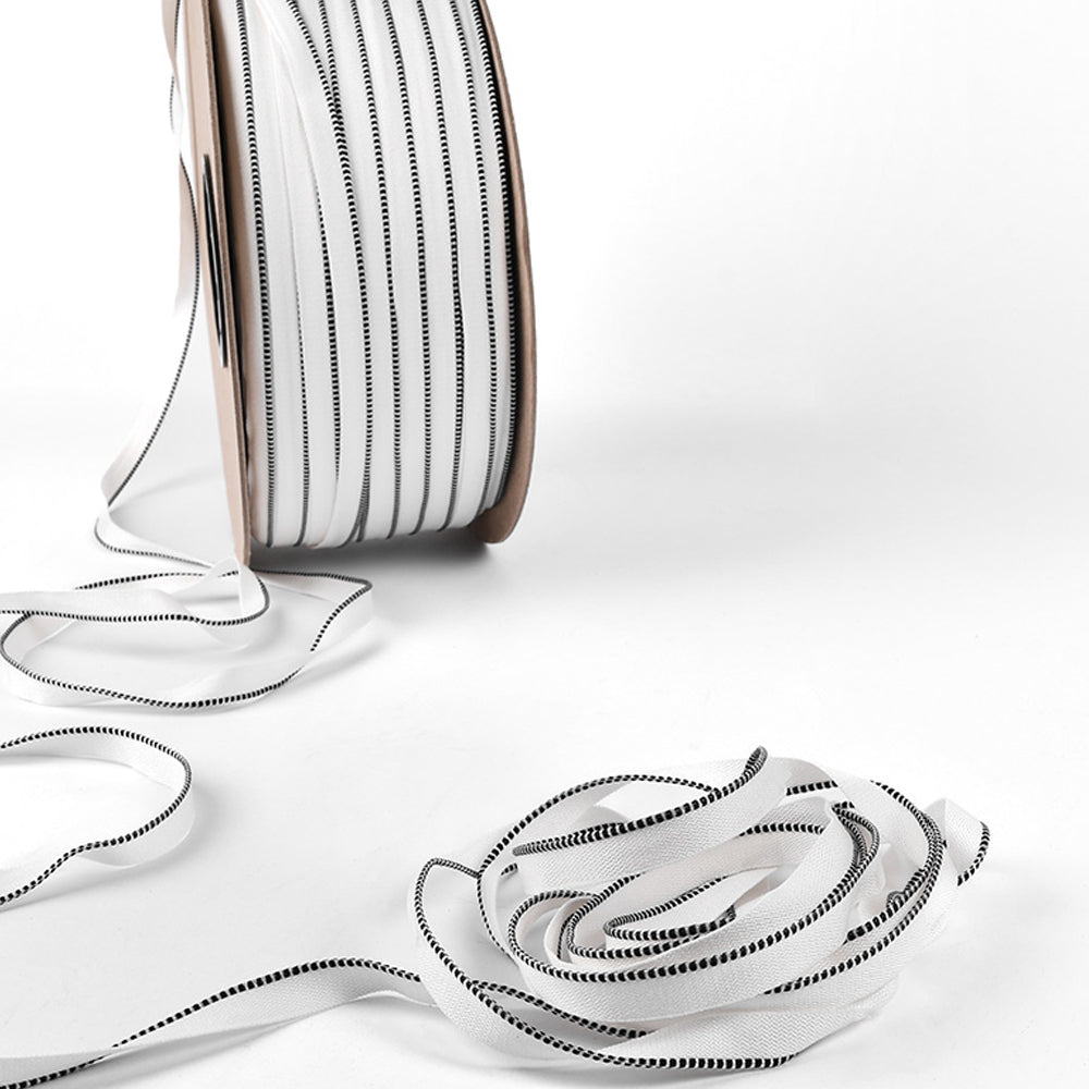 Spule mit weißem Alexandra-Renke-Band mit schwarz abgesteppten Kanten, teilweise auf weißer Fläche abgerollt - ideal, um Buchrücken von Hardcover-Büchern zu veredeln.