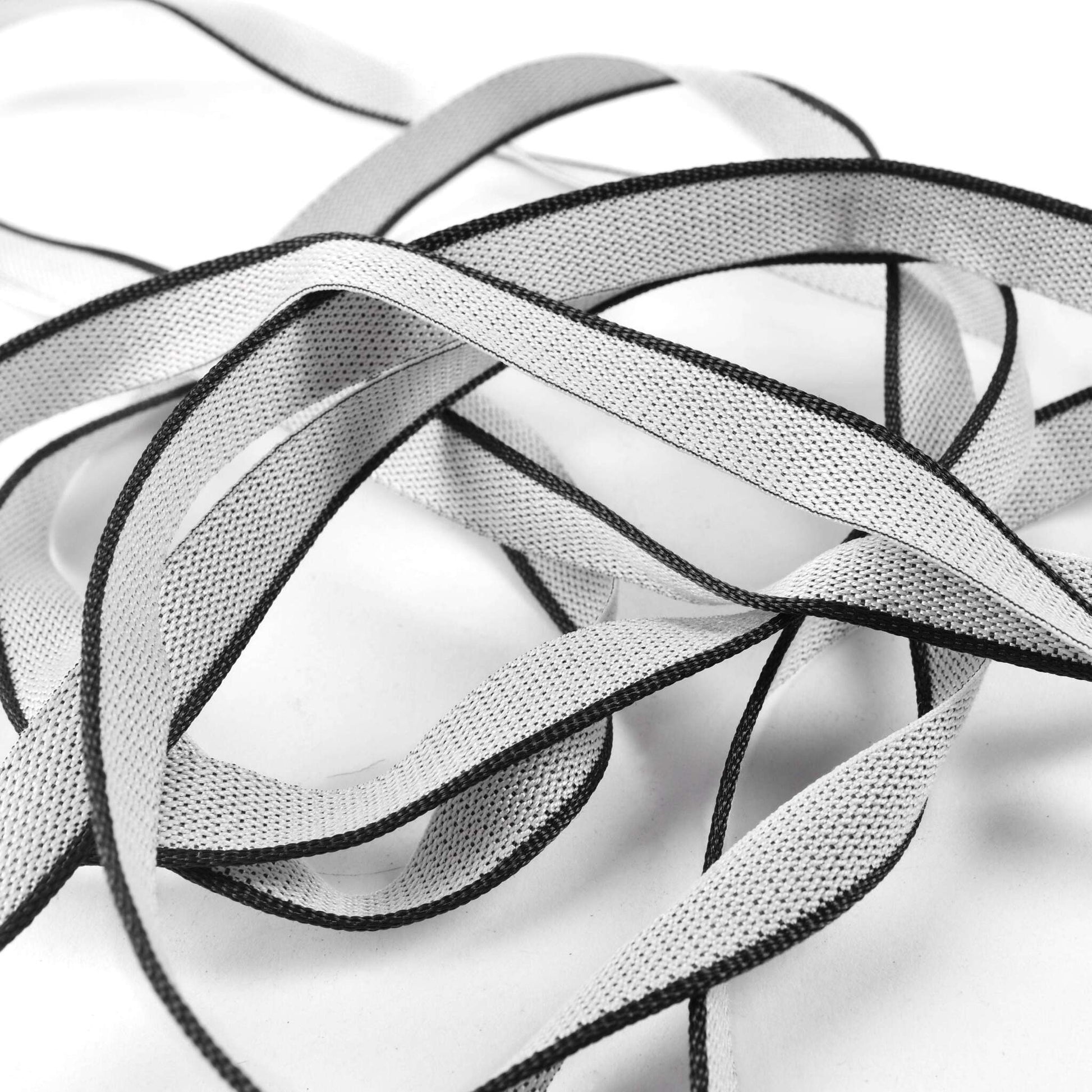 Graue und schwarze flache Schnürsenkel von Alexandra Renke, die an einen Kapitalband aus Hardcover-Büchern erinnern, sind auf weißem Grund miteinander verflochten.