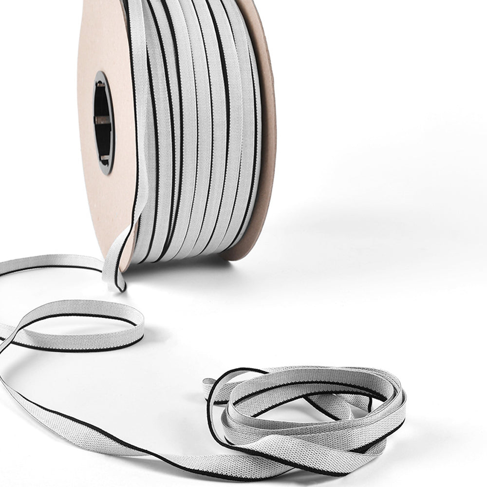 Eine Spule Alexandra Renke Reflexband mit einer losen Länge, die auf einer weißen Oberfläche aufgerollt ist - ideal, um Buchrücken zu akzentuieren oder Ihren Hardcover-Büchern einen klassischen Kapitalband-Stil zu verleihen.