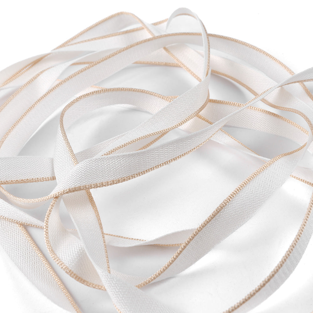 Das Kapitalband aus weißem Satin von Alexandra Renke mit hellen Goldrändern, locker gewickelt auf weißem Grund - ideal, um Hardcover oder Buchrücken einen raffinierten Akzent zu verleihen.