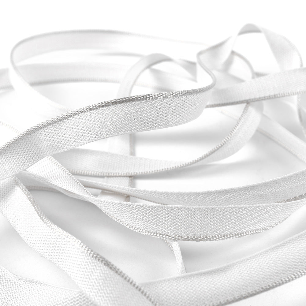 Alexandra Renke weiße, flache, elastische Bänder, ähnlich dem Kapitalband in Hardcover-Büchern, sind locker gewickelt und überlappen sich auf einem schlichten weißen Hintergrund.