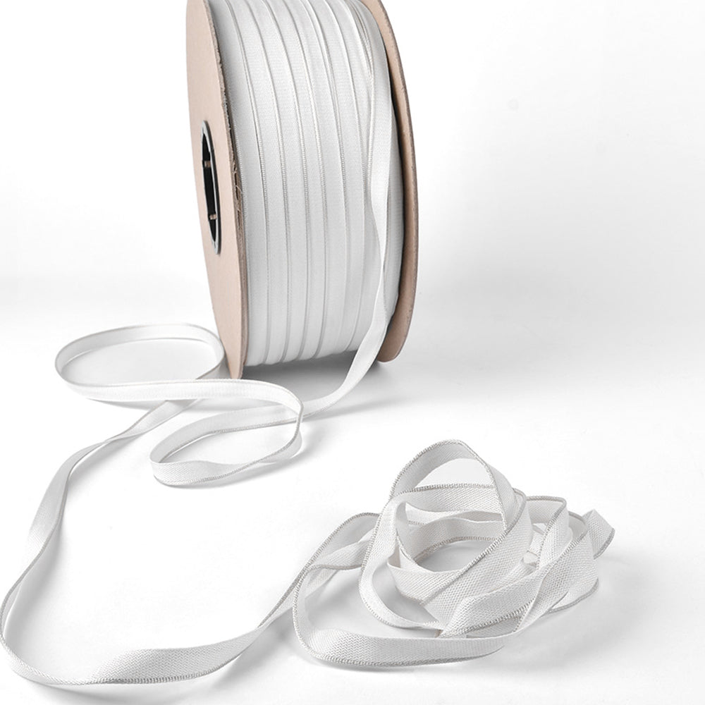 Eine Spule mit weißem Gummiband von Alexandra Renke, das üblicherweise als Kapitalband für gebundene Buchrücken verwendet wird, wobei ein Teil des Bandes abgerollt und lose auf einen weißen Hintergrund aufgewickelt ist.