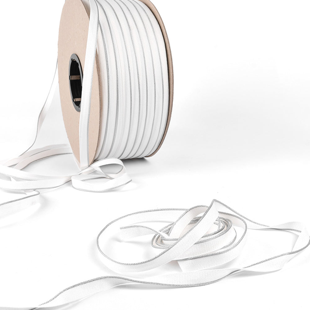 Eine Spule mit weißem Gummiband von Alexandra Renke, perfekt für die Reparatur von Buchrücken oder als Kapitalband in Hardcover-Büchern, mit etwas abgewickeltem Band auf einer weißen Fläche.