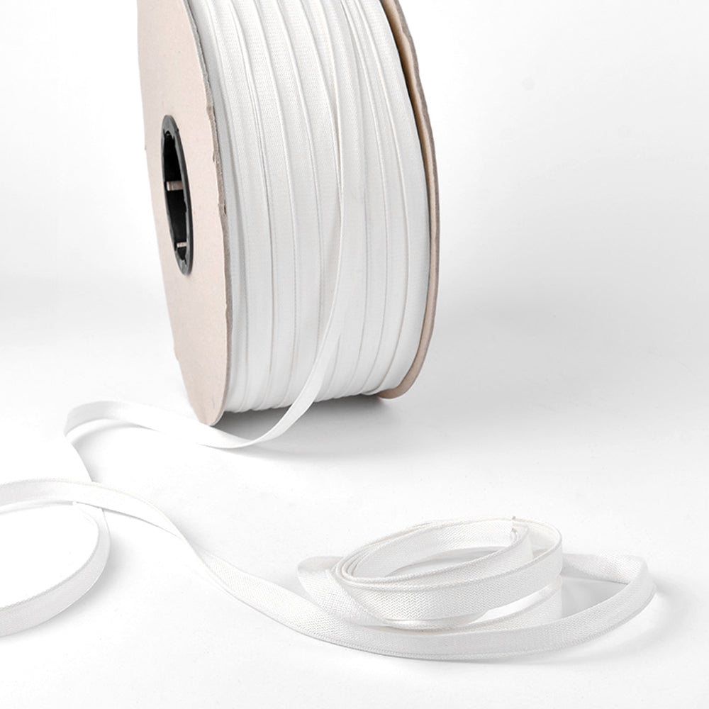 Eine Spule mit weißem Gummiband von Alexandra Renke, das üblicherweise als Kapitalband für Buchrücken in Hardcover-Büchern verwendet wird, mit etwas loser Länge auf weißem Hintergrund.