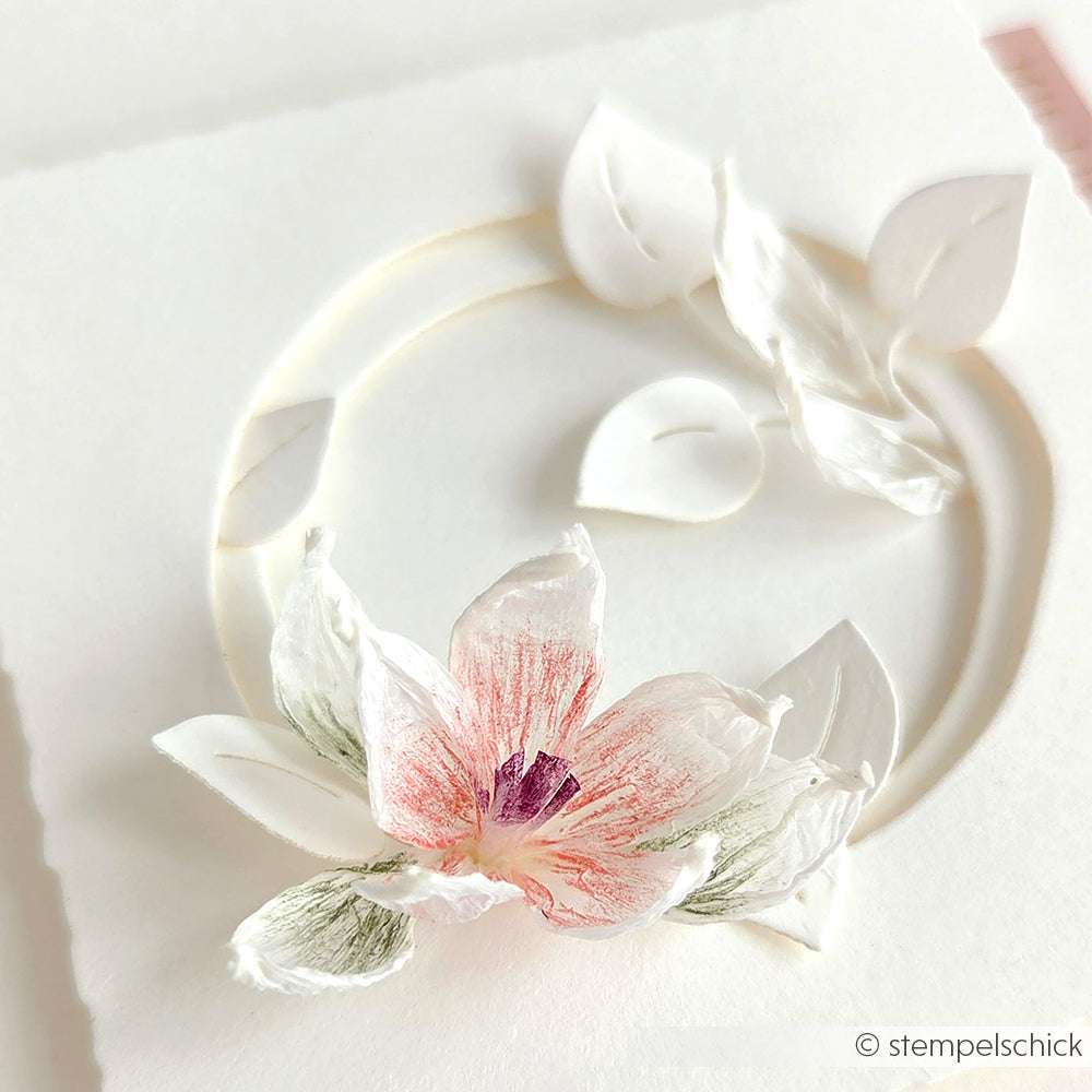 Eine zarte, dreidimensionale Papierblume von Paperphine mit rosa und grünen Details auf einer weißen Karte - ideal für Bastelprojekte oder als elegante Ergänzung zu Ihrer nächsten Papierschnur-Kreation.