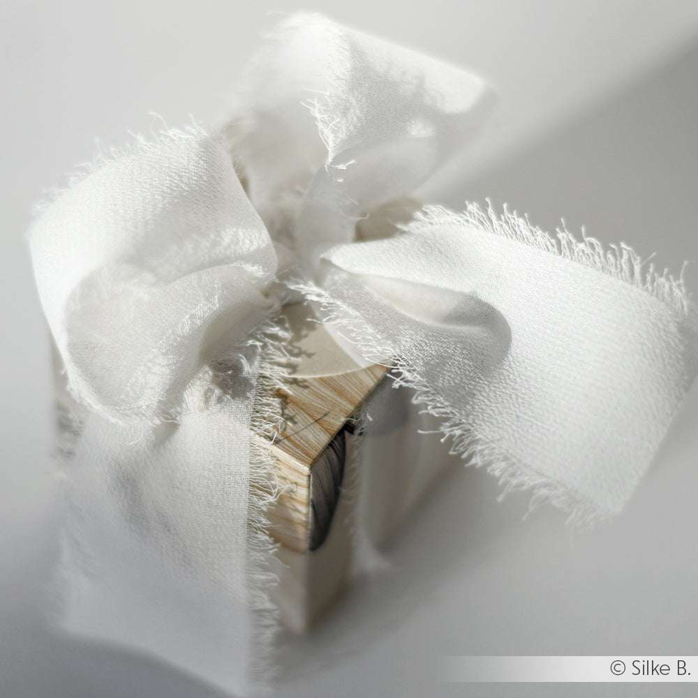 Kleine Geschenkschachtel, umwickelt mit einem rustikalen weißen Stoffband von Vivant Decorations BV, gebunden mit einer großen, ausgefransten Schleife - ideal für Deko Ideen oder kreative Bastelprojekte.