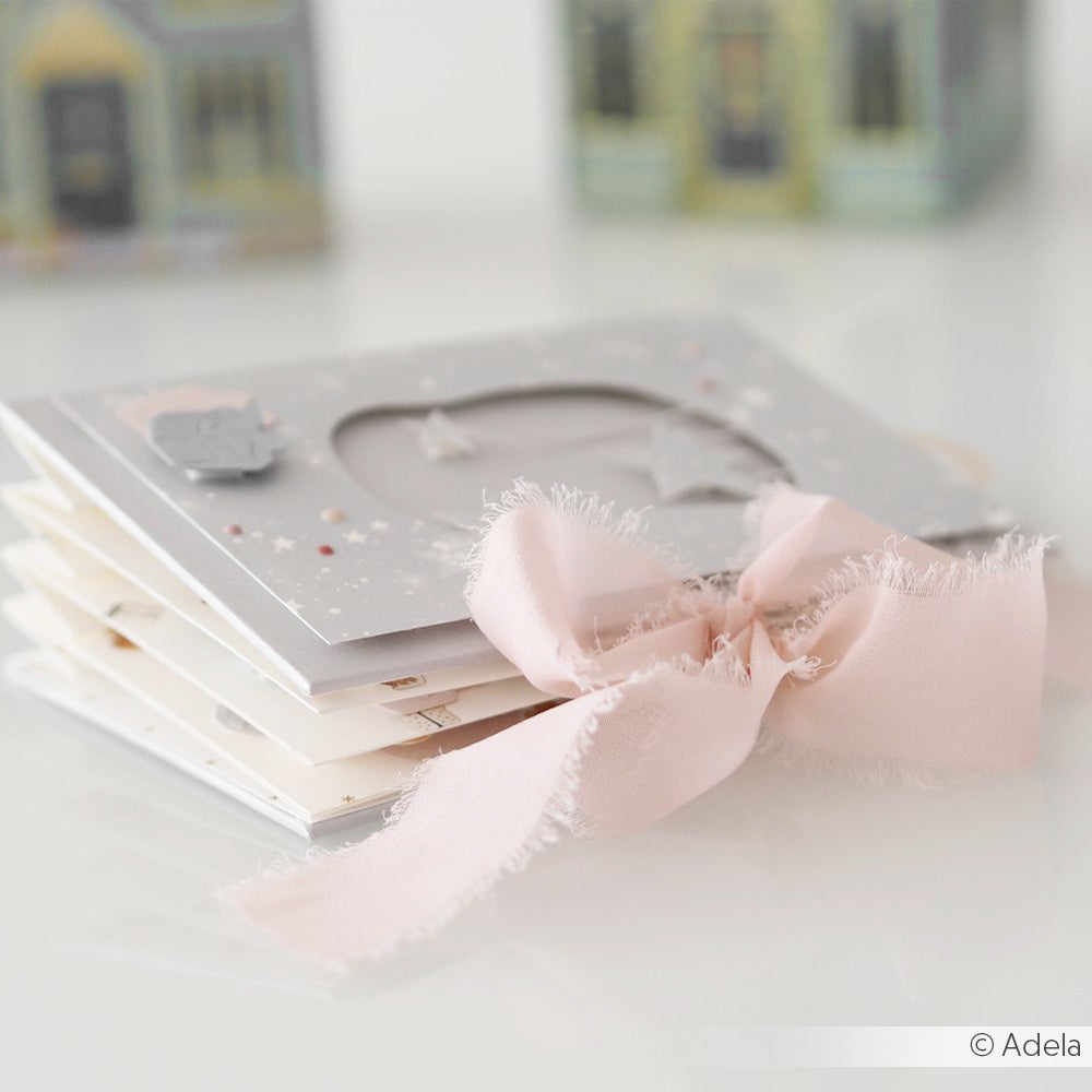 Ein Stapel handgefertigter Karten, gebunden mit einem ausgefransten rosa Chiffonband von Vivant Decorations BV, mit dekorativen Häusern im Hintergrund - perfekt für Bastelprojekte oder einzigartige Deko Ideen.