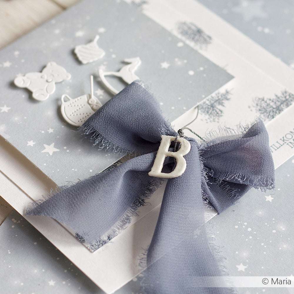 Eine graue Chiffonschleife von Vivant Decorations BV mit einem weißen Buchstaben B, gestylt auf sternförmigem Papier und akzentuiert mit kleinen weißen Anhängern - ideal für Bastelprojekte oder kreative Deko Ideen.